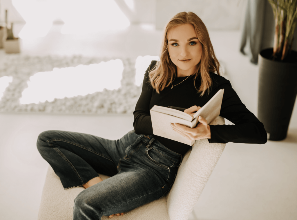 Psychoterapeutka Weronika Grzelak siedząca w salonie na białym krześle i czytająca książkę